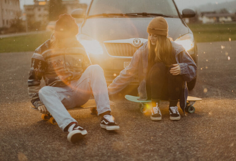 Paar sitzt auf Skateboard vor einem Auto in der Dämmerung