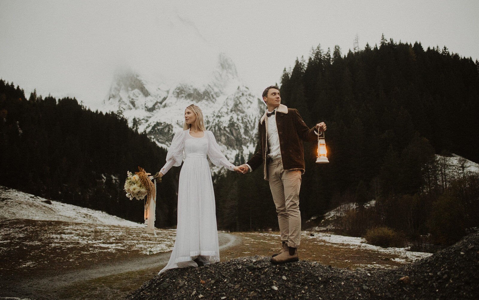 Elopement Fotoshooting von einem Vintage Hochzeitspaar in der Schweiz beim Rosenlaui. Brautpaar hält Petroliumlampen in der Hand und im Hintergrund ist das Rosenlaui mit Schnee.