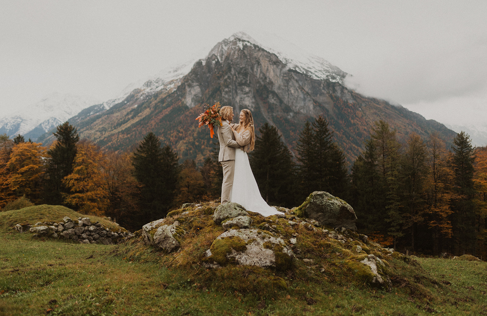 Hochzeits Fotoshooting mit einem Brautpaar in den Bergen. Paar steht auf einem Stein mit einem grossen Berg im Hintergrund. Meiringen Schweiz.
