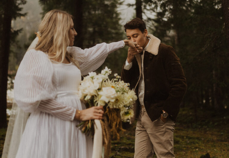 Mann küsst die Hand der Braut an ihrem Elopement in den Schweizer Bergen. Braut trägt ein Vintage Kleid und hält einen schönen weissen Blumenstrauss in der Hand.