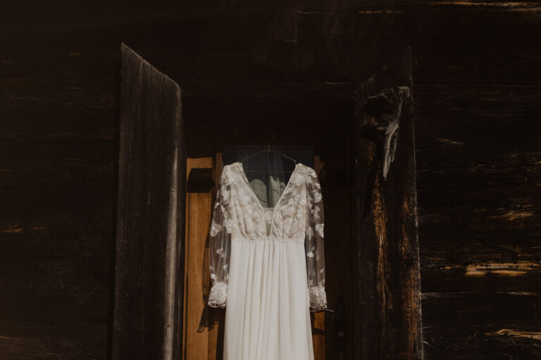 boho Hochzeitskleid hängt an einer Türe eines Walliser Chalet in den Bergen.