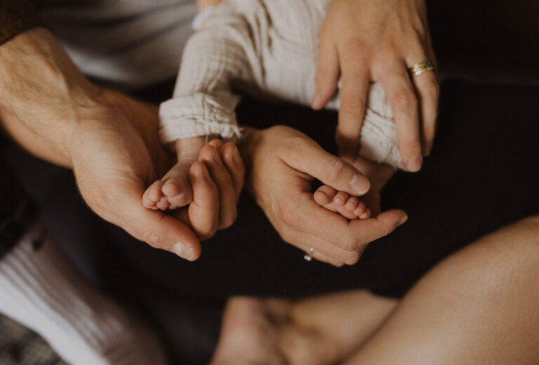 Hände der Eltern halten die Baby Füsse von ihrem neugeborenem Sohn