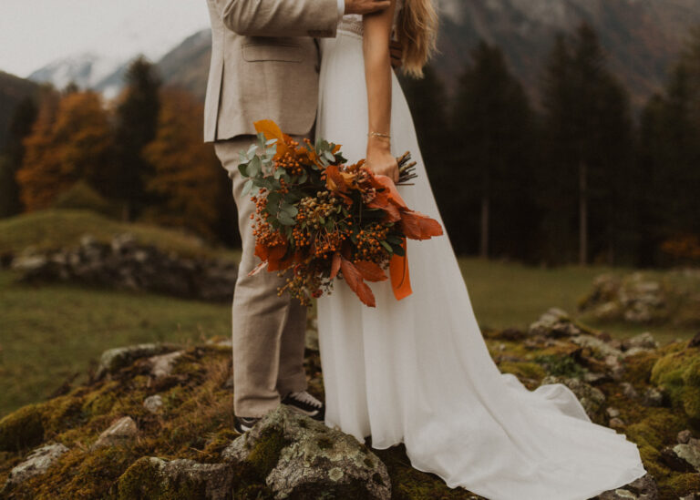 Hochzeitspaar in den Schweizer Bergen am Hochzeitsfotos machen im Herbst. Oranger Blumenstrauss
