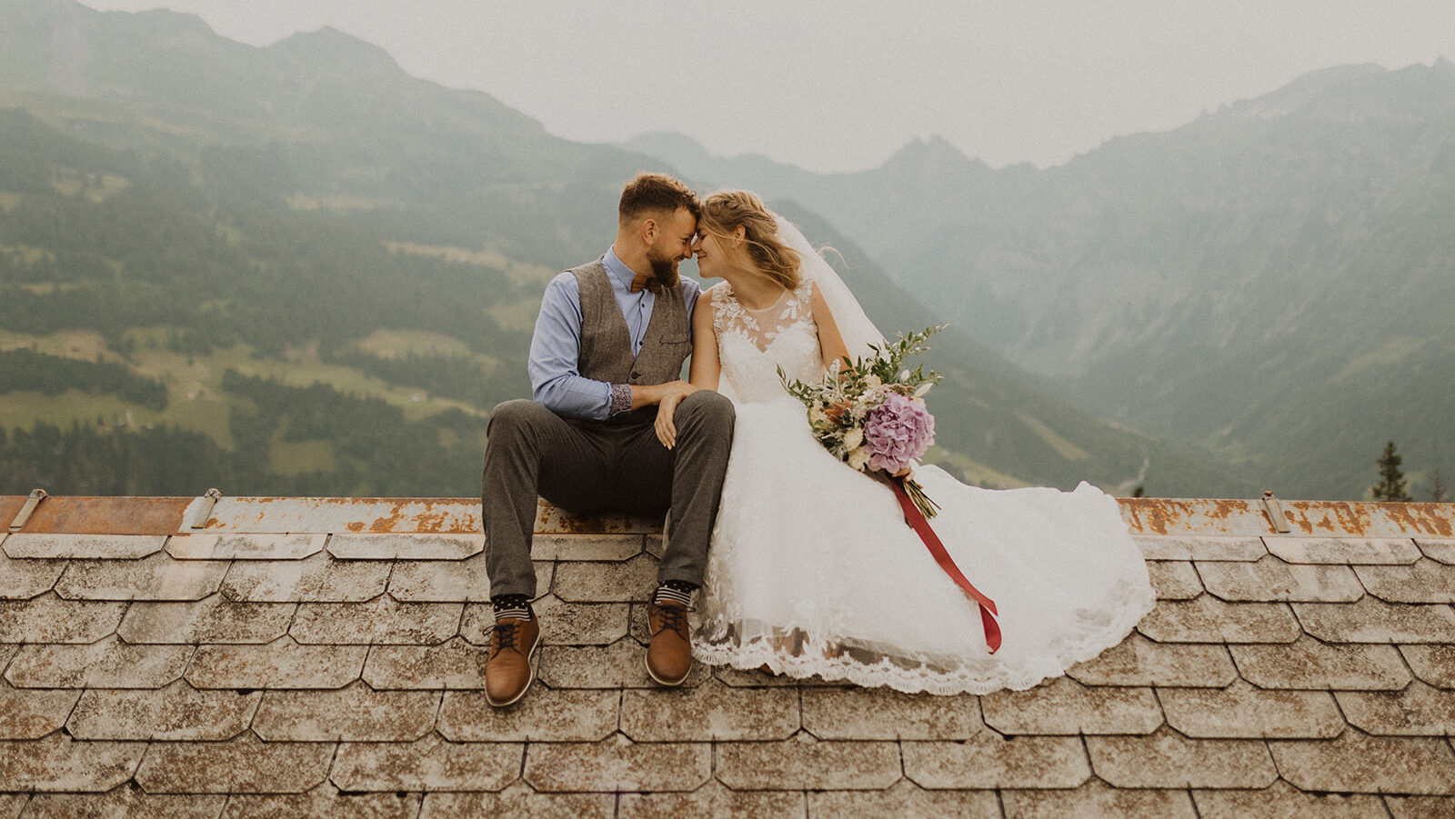 Berghochzeit im Glarnerland im Kanton Schwyz. Brautpaar sitzt auf dem Dach einer Berghütte.