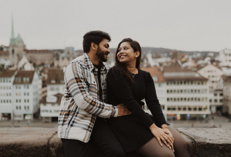 Paar sitzt auf einer Mauer mit Blick auf die Stadt Zürich.