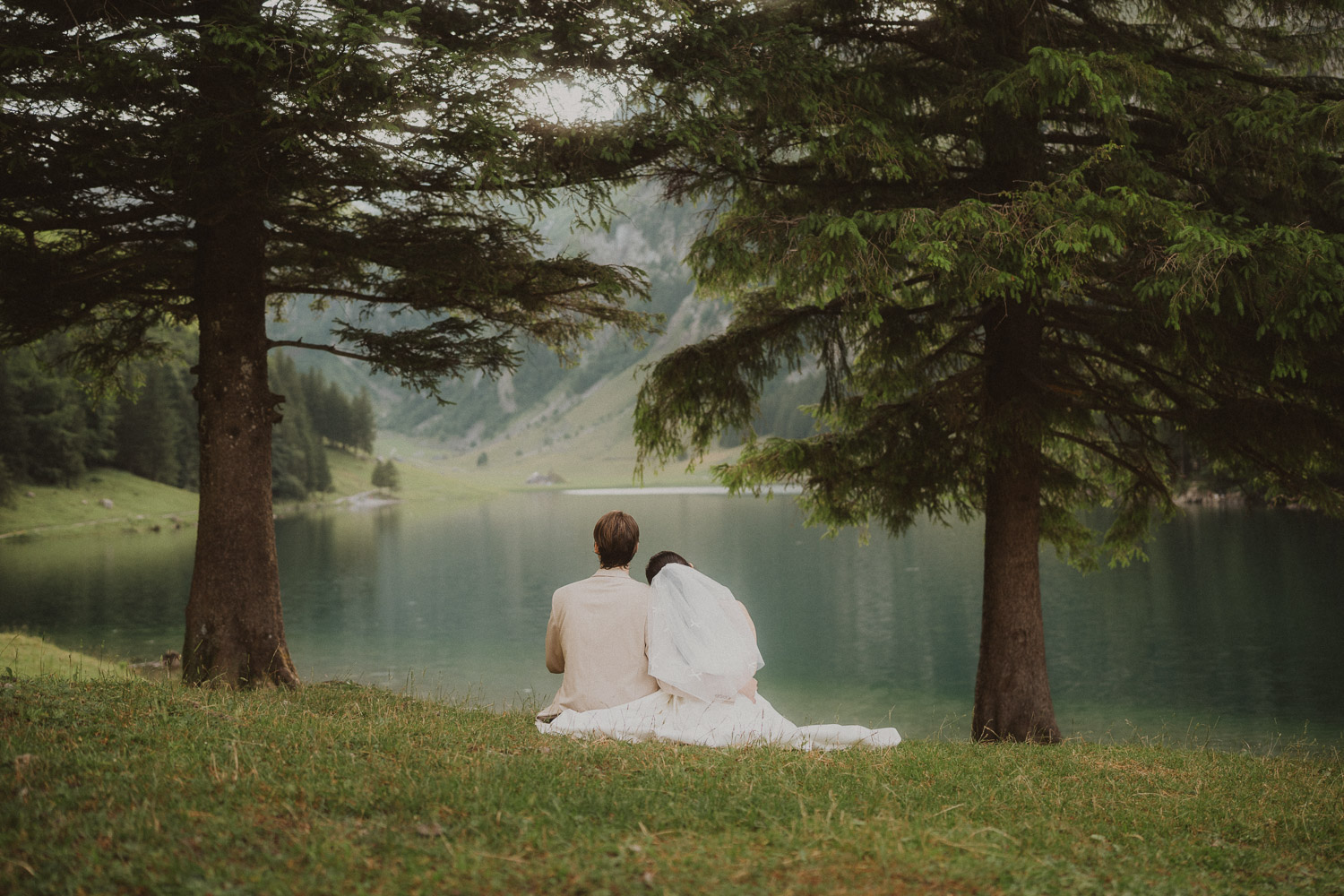 Couple eloping and sitting in the grass at Seealpsee in Appenzell, photographed by an elopement and proposal photographer.