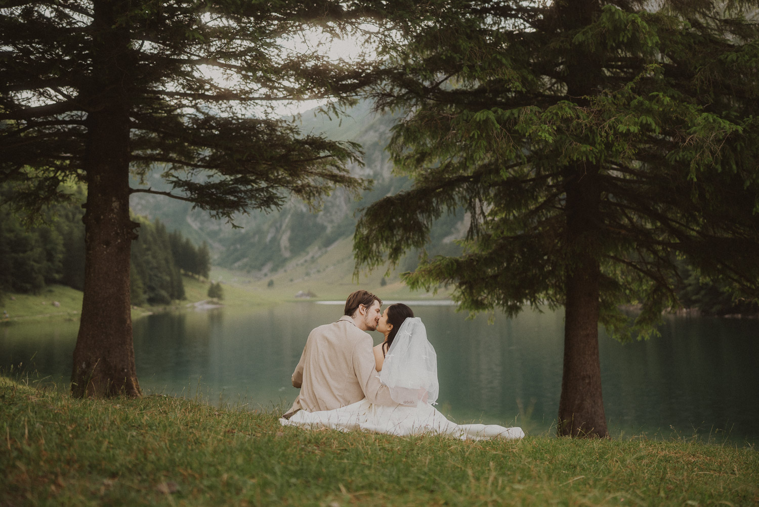 Elopement couple sitting in the grass and kissing at Seealpsee in Appenzell, photographed by an elopement and proposal photographer.
