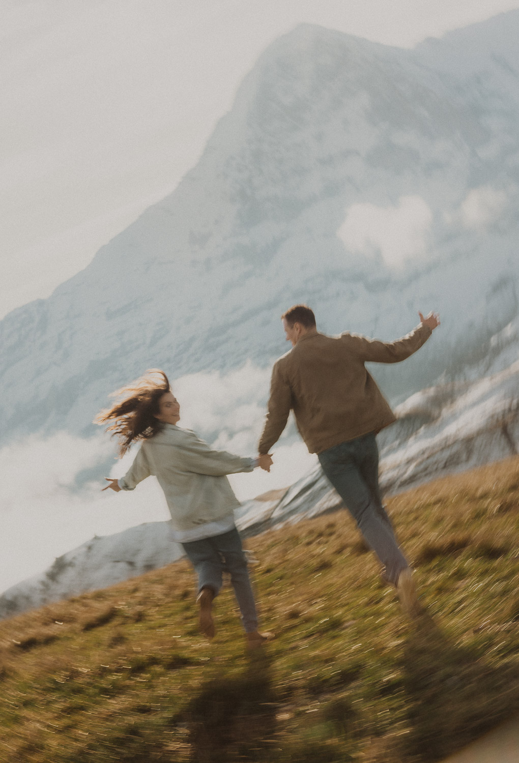 Couple running at a surprise proposal photography session in the Jungfrauregion with alpine mountain scenery and natural outdoor setting in daylight.