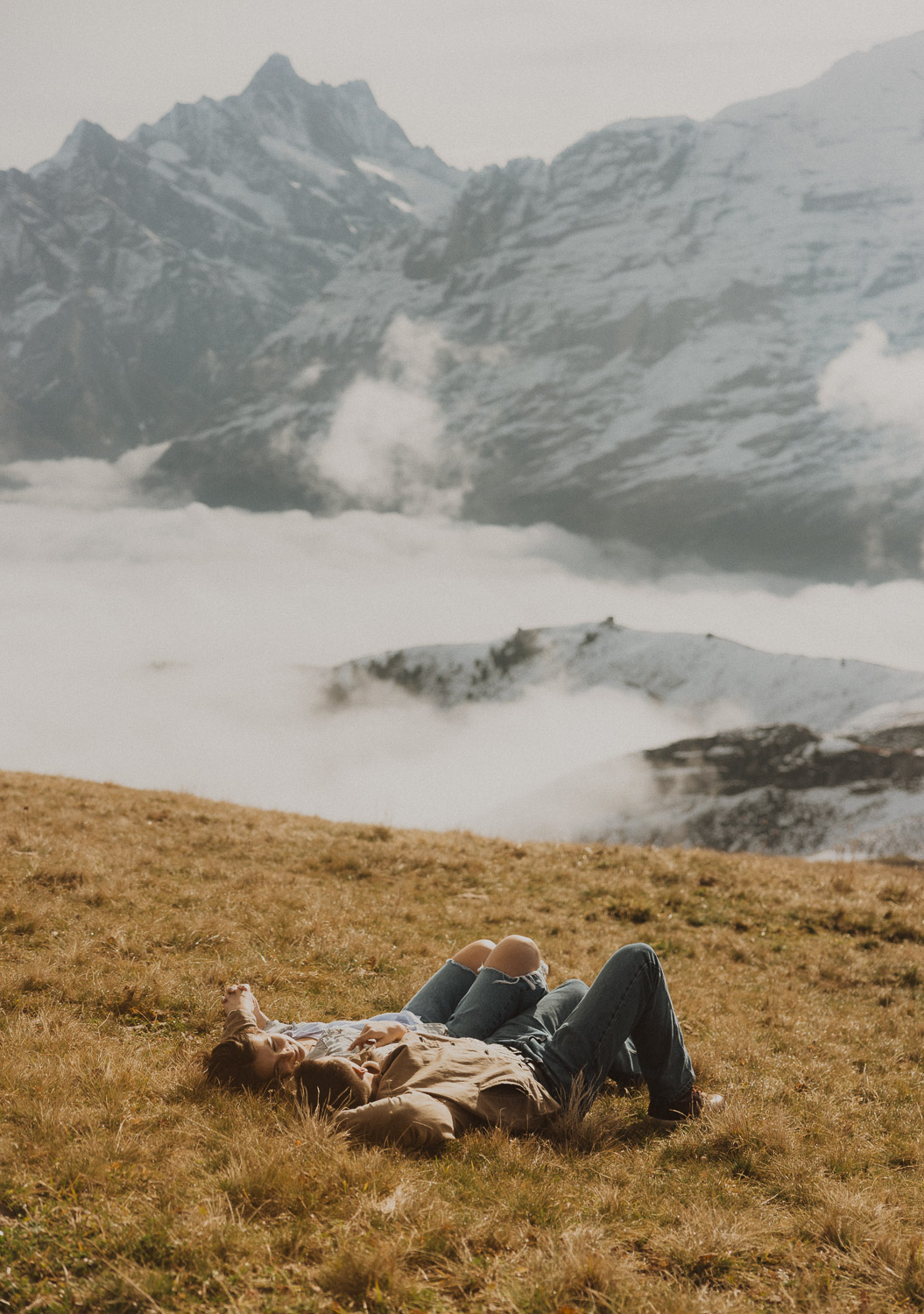 Couple laying in the grass at a surprise proposal photography session in the Jungfrauregion with alpine mountain scenery and natural outdoor setting in daylight.