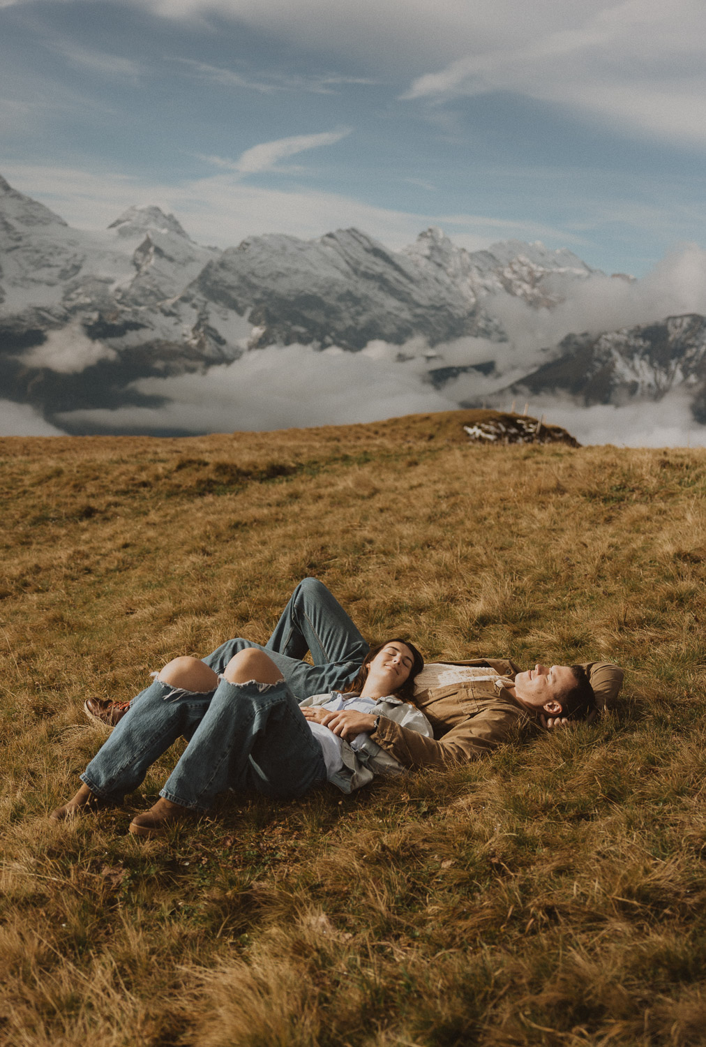 Couple laying in the grass at a surprise proposal photography session in the Jungfrauregion with alpine mountain scenery and natural outdoor setting in daylight.