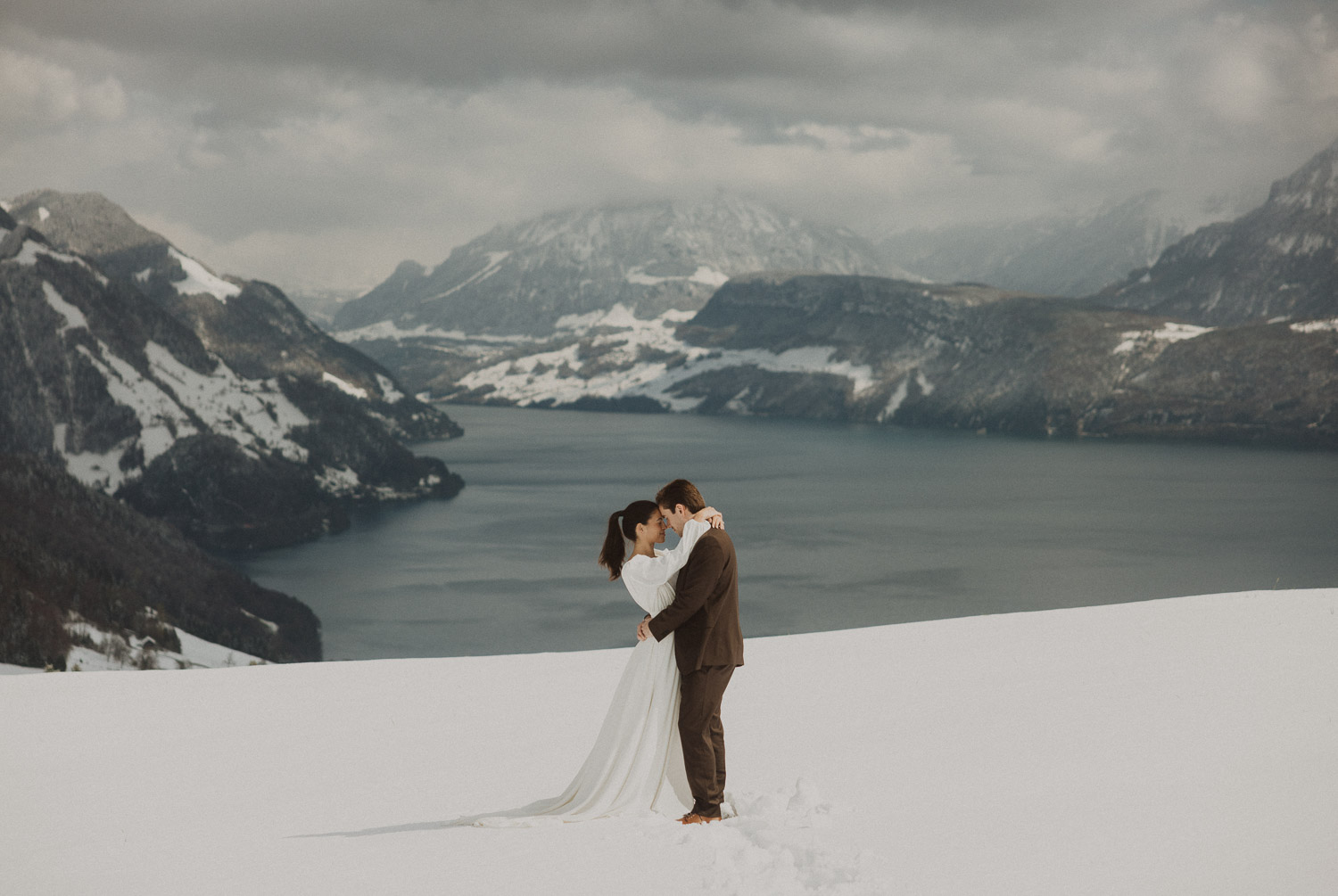 Couple during an elopement photography session in Lucerne with snow-covered alpine mountains and a lakeside backdrop.