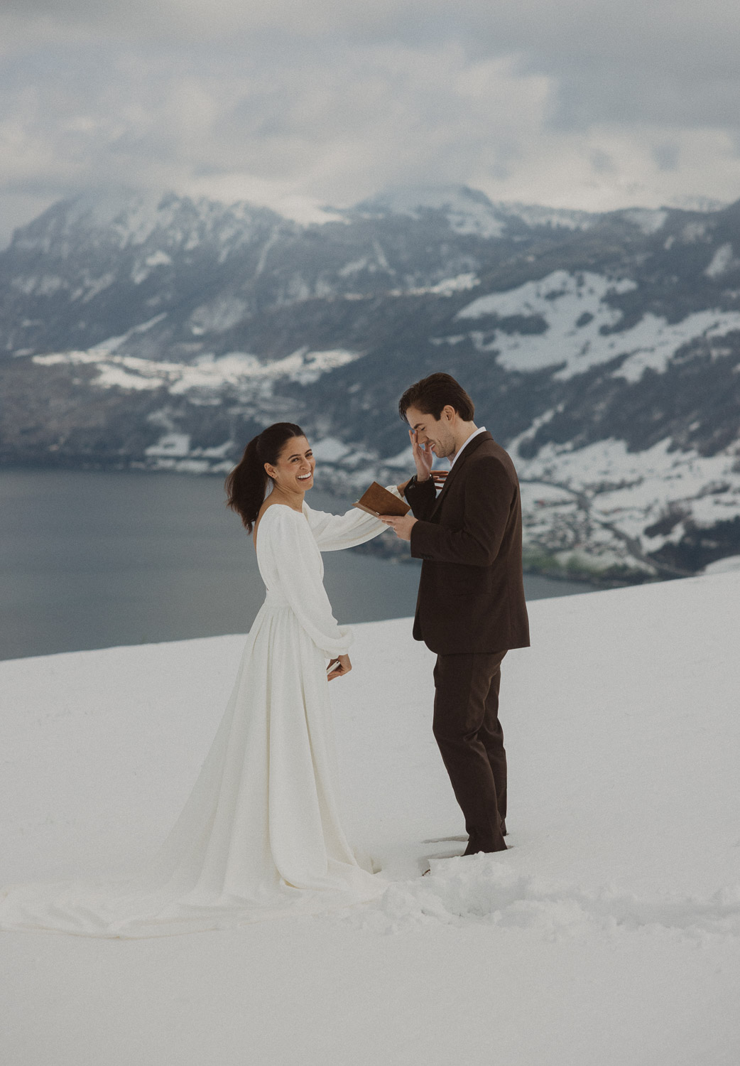 Couple exchanging vows on an elopement photography session in Lucerne with snow-covered alpine mountains and a lakeside backdrop.