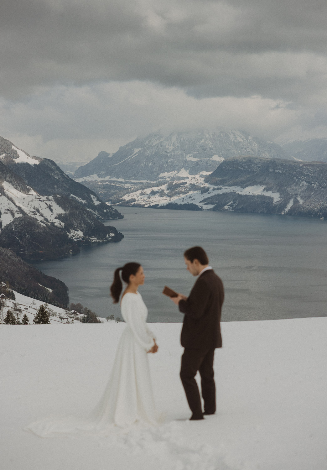 Couple exchanging vows on an elopement photography session in Lucerne with snow-covered alpine mountains and a lakeside backdrop.