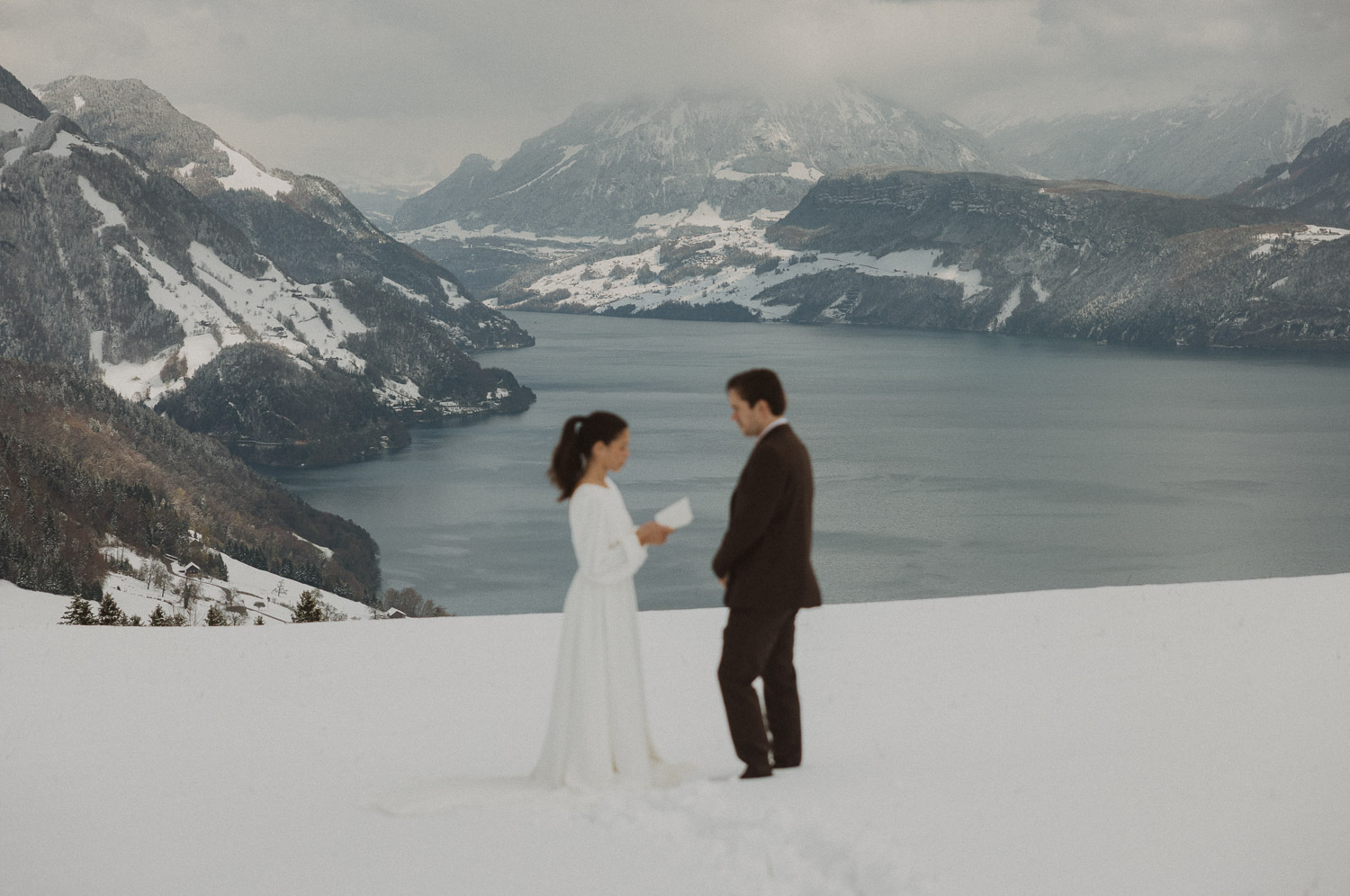 Couple exchanging vows on an elopement photography session in Lucerne with snow-covered alpine mountains and a lakeside backdrop.