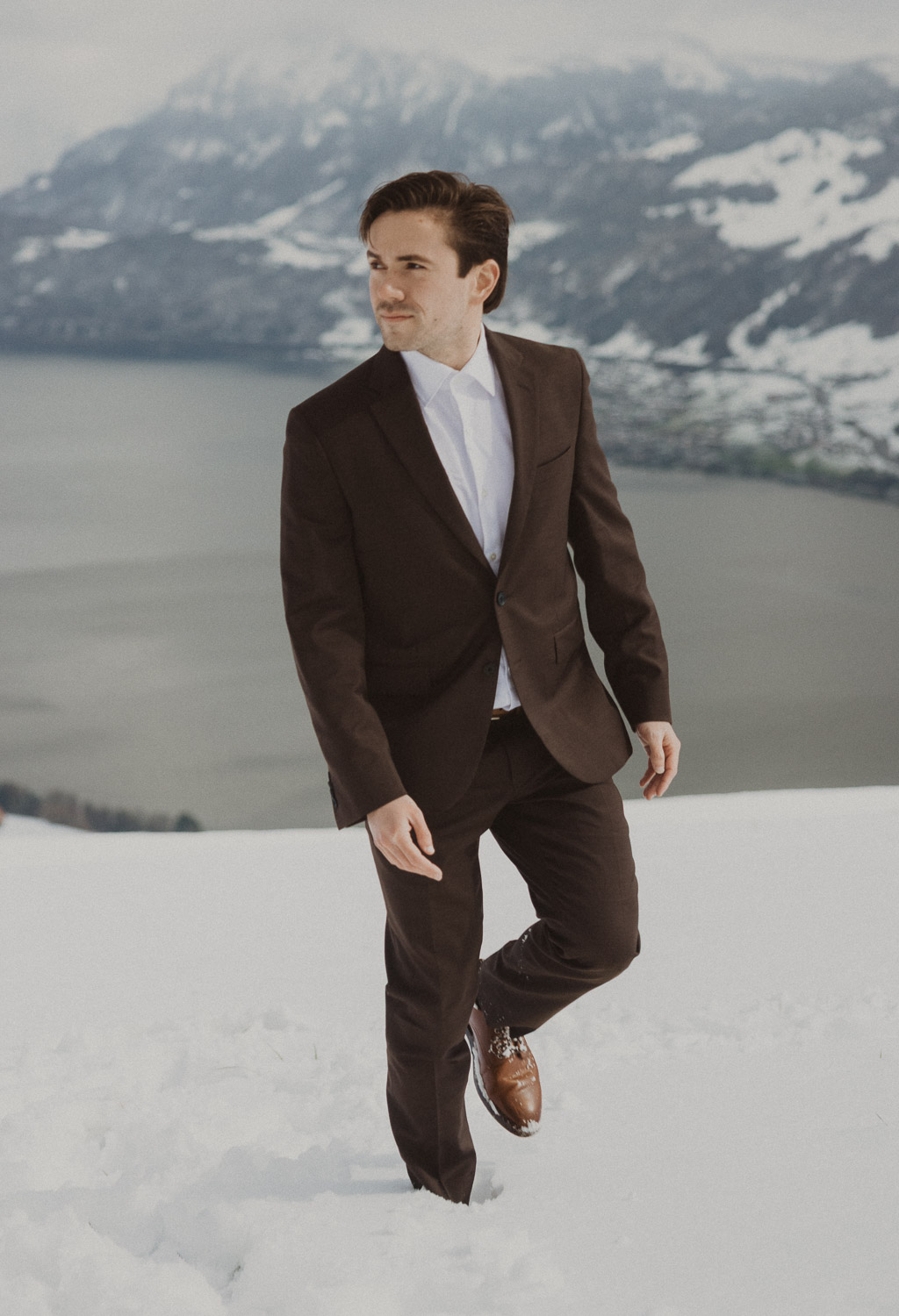 Groom during an elopement photography session in Lucerne with snow-covered alpine mountains and a lakeside backdrop.